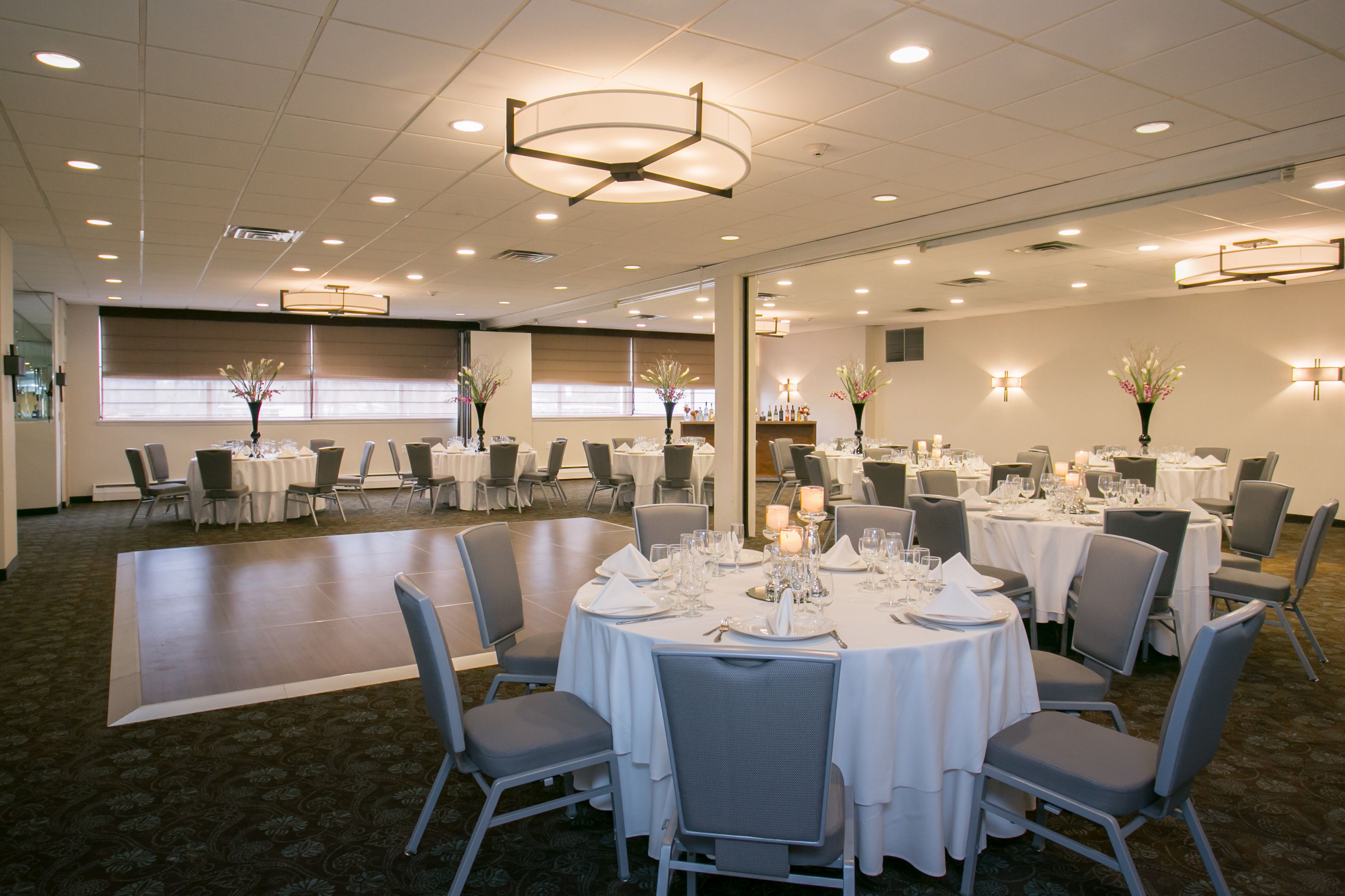 A spacious banquet hall with round tables set for dining, equipped with chairs and table settings.