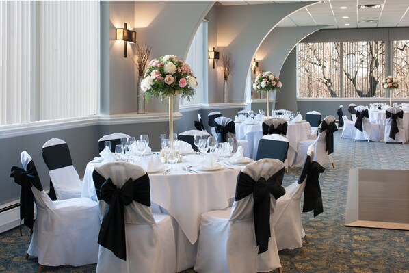 A banquet hall with round tables, black and white chairs, and floral centerpieces.