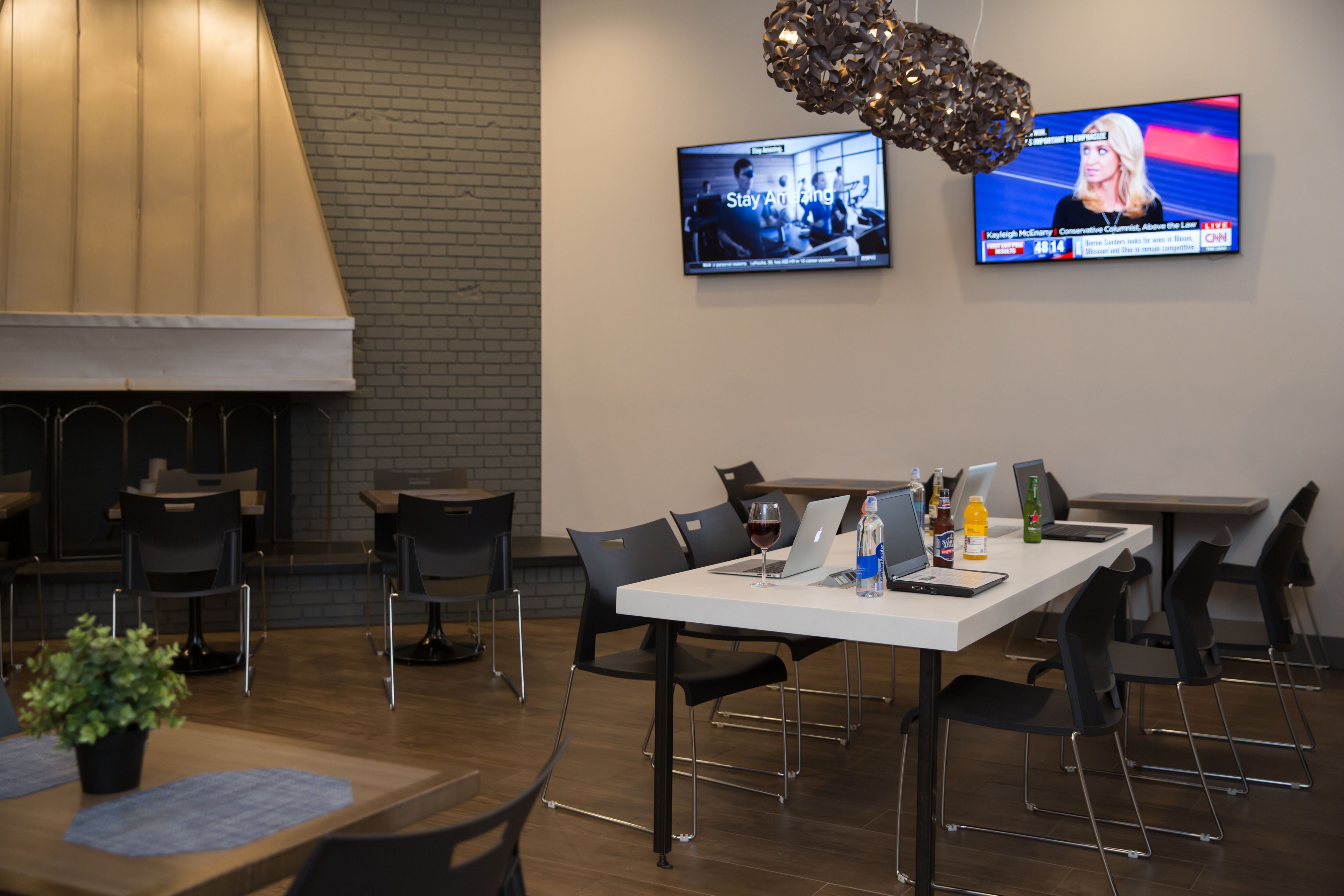 A modern conference room with a white table, black chairs, a TV displaying a news program, and a decorative light fixture.