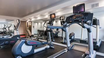 A gym with cardio machines, weight training equipment, and a mirrored wall.