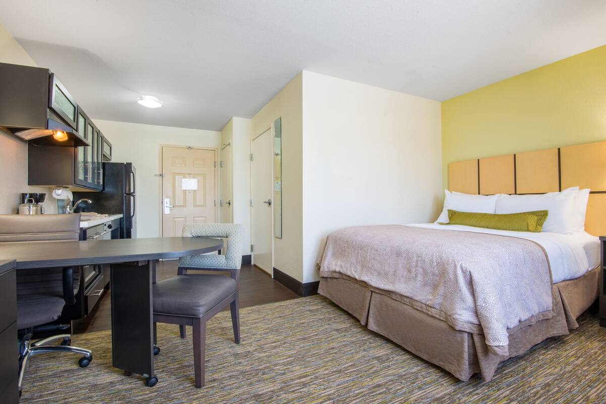 Een hotelkamer met een bed, een bureau, een stoel, een kitchenette en een badkamer.