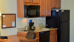 A compact kitchen with wooden cabinets, a black microwave, a black refrigerator, a coffee maker, and a dishwasher. - Candlewood Suites Jefferson City by IHG (Jefferson City)