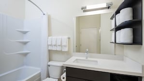 A modern bathroom with a bathtub, toilet, sink, and a towel rack with multiple towels. - Candlewood Suites Jefferson City by IHG (Jefferson City)