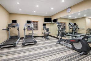 Un gimnasio con cintas de correr, elípticas y un espejo grande.