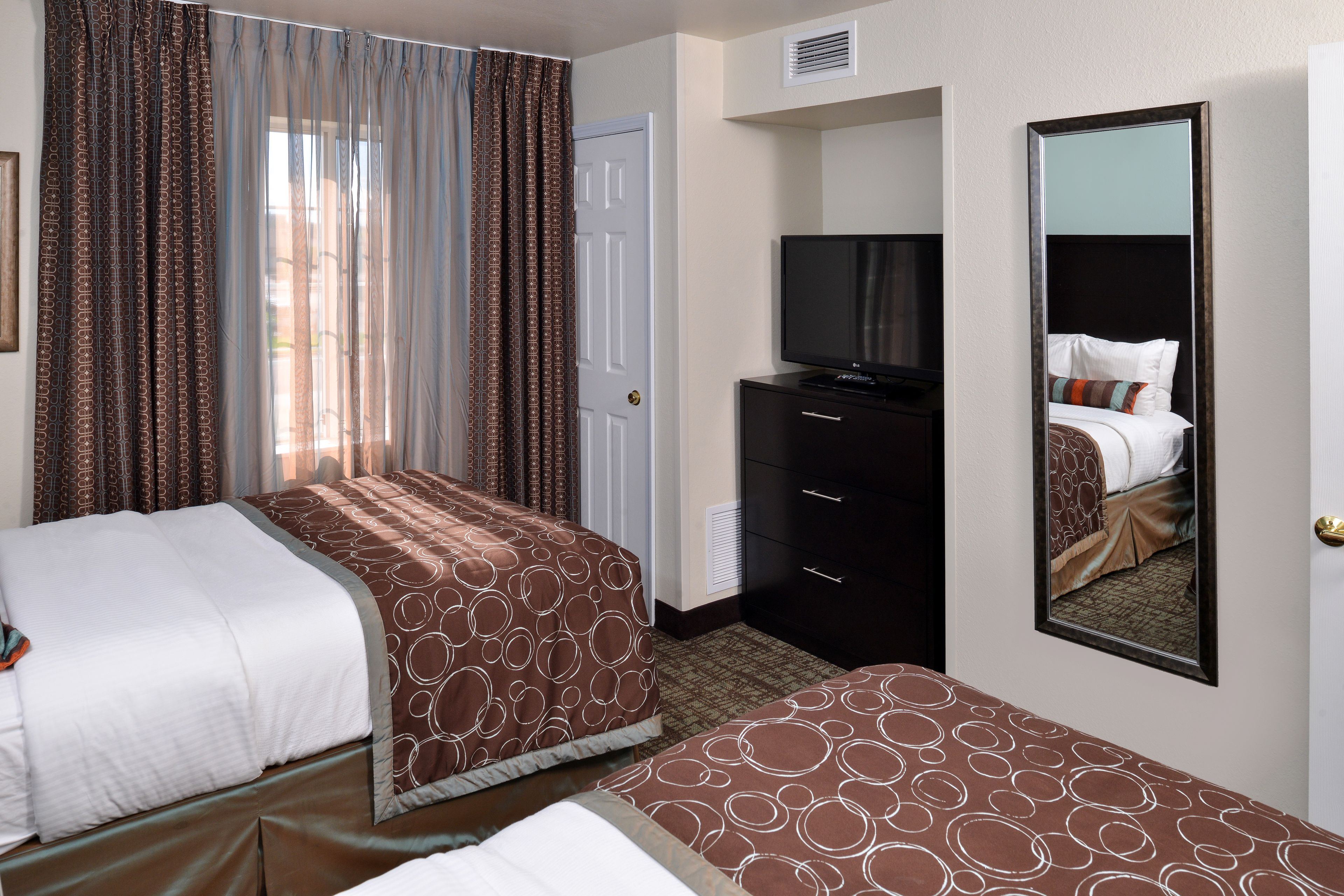 A hotel room with two beds, a TV, a dresser, and a mirror.