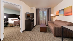 A hotel room with a bed, a TV, a sofa, a small table, and a window with curtains. - Staybridge Suites Sioux Falls by IHG (Sioux Falls)