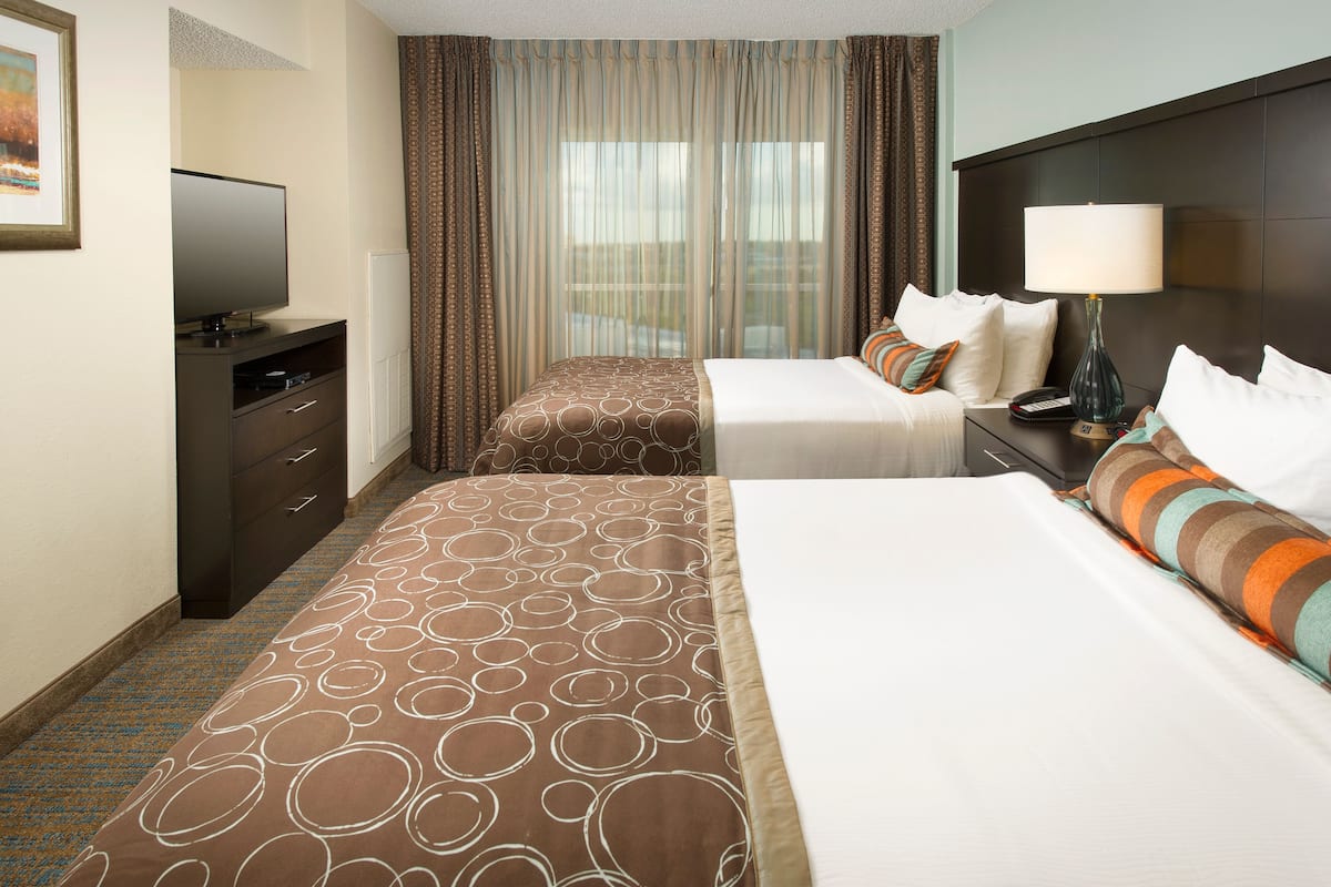 A hotel room with two beds, a TV, a desk, and a lamp.