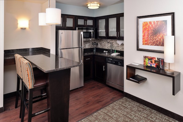 A modern kitchen with a central island, stainless steel appliances, dark cabinetry, and a small countertop with a magazine rack.