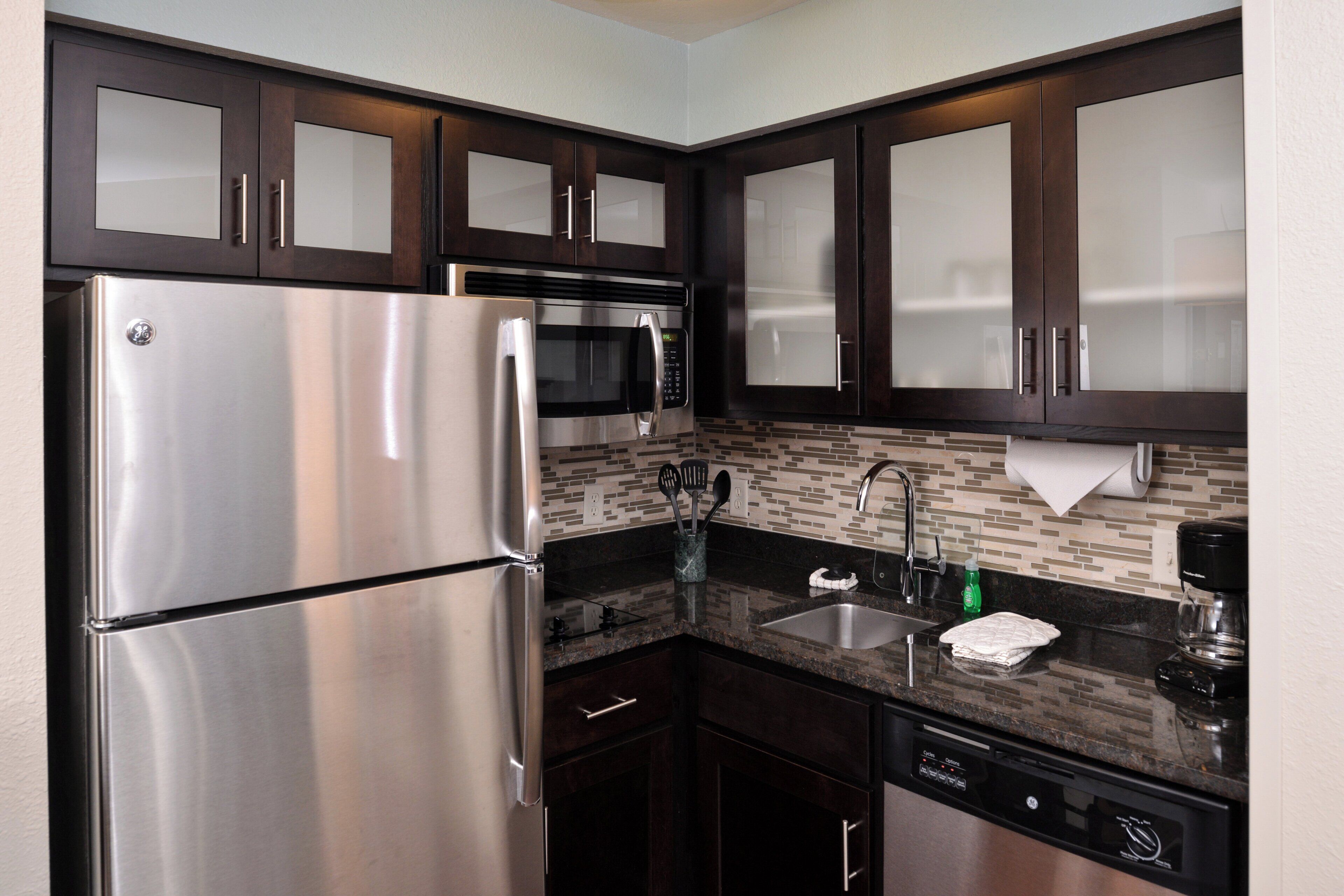 Una cocina moderna con electrodomésticos de acero inoxidable, armarios de madera oscura, salpicadero de azulejos y lavavajillas empotrado.