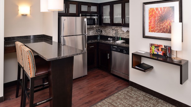 A modern kitchen with dark wood cabinets, stainless steel appliances, and a bar area with a bar stool. - Staybridge Suites Sioux Falls by IHG (Sioux Falls)