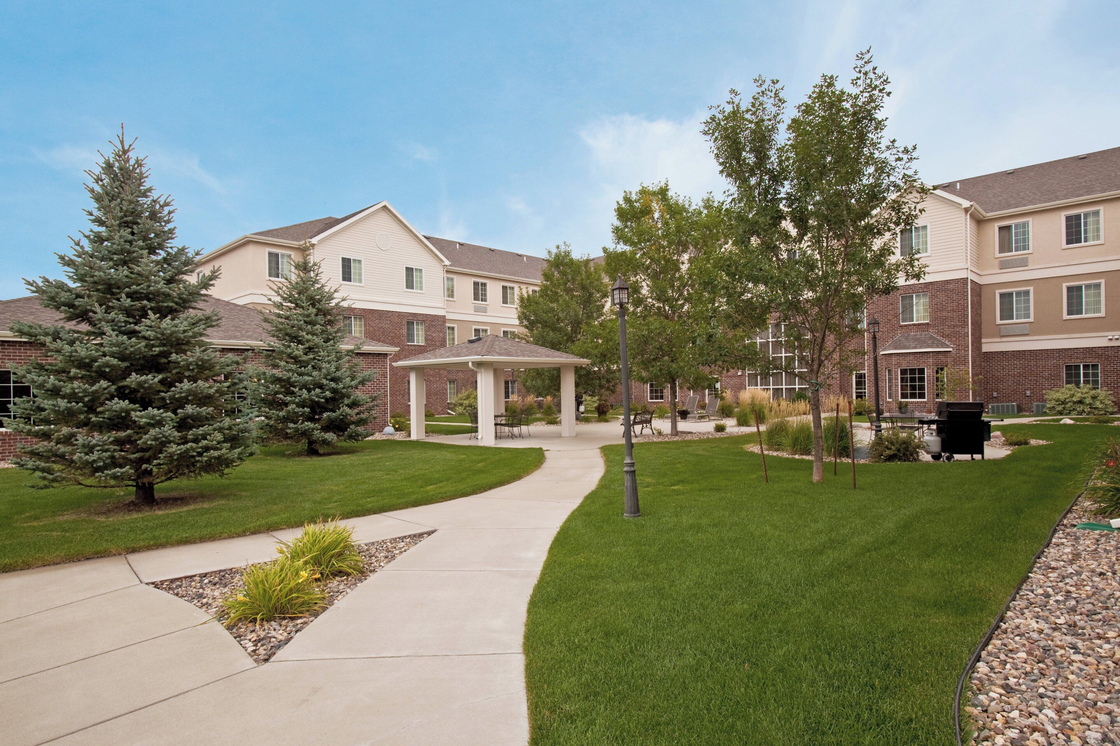 A residential building with a covered patio, a lawn, and a pathway leading to the entrance.
