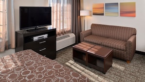 A hotel room with a flat-screen TV, a sofa, a coffee table, and a patterned bedspread. - Staybridge Suites Sioux Falls by IHG (Sioux Falls)