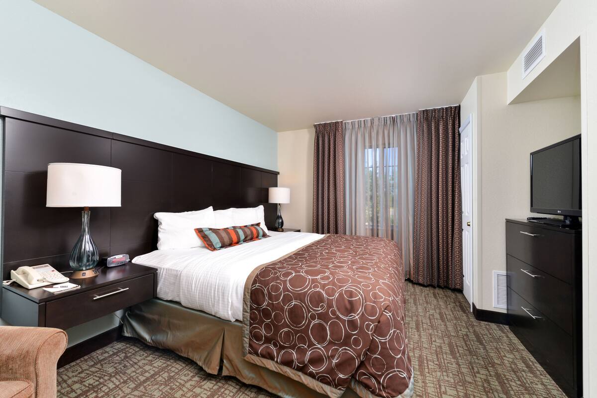 A hotel room with a large bed, two bedside tables with lamps, a television, and a wardrobe.