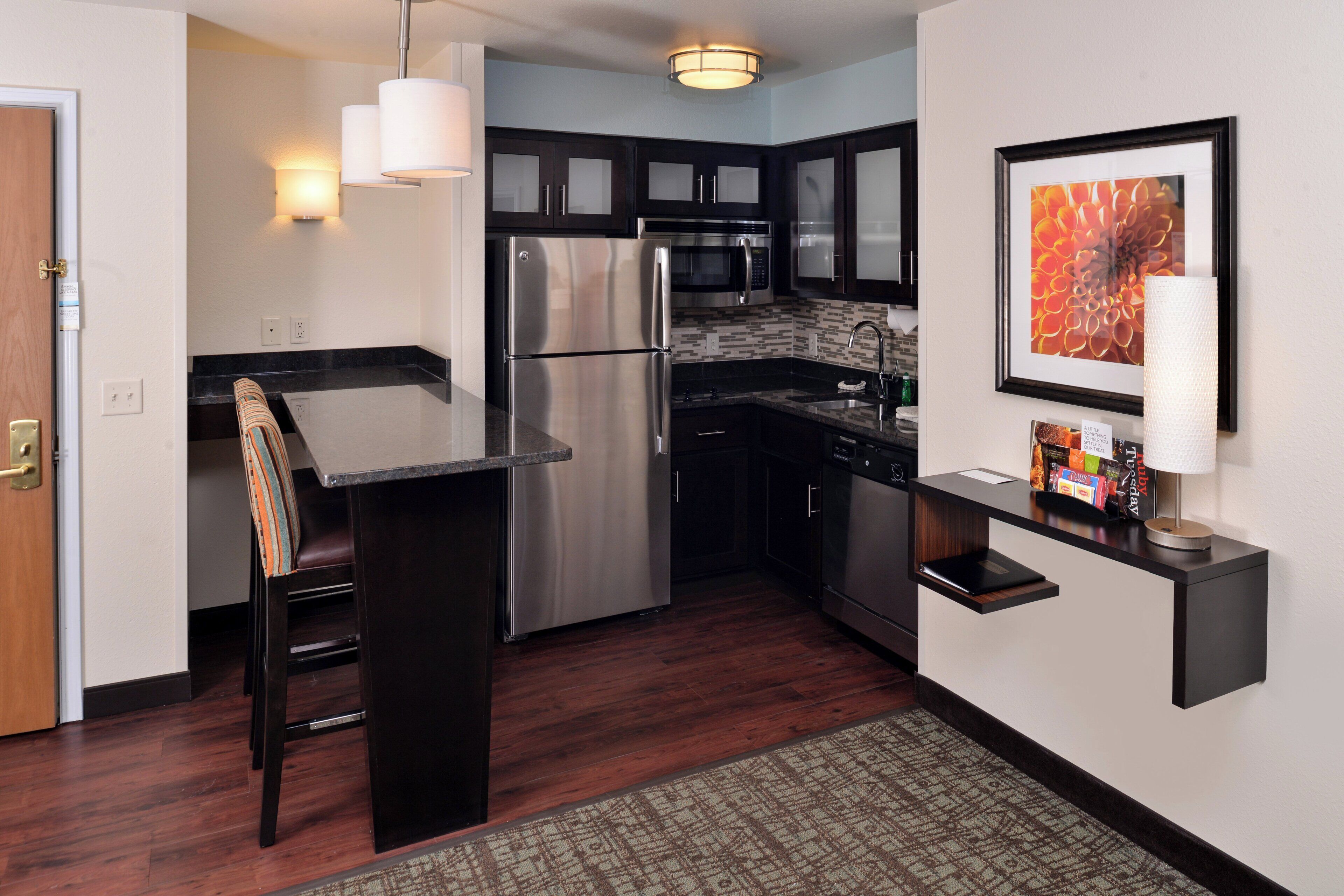 A modern kitchen with dark cabinetry, stainless steel appliances, and a small island with a chair.