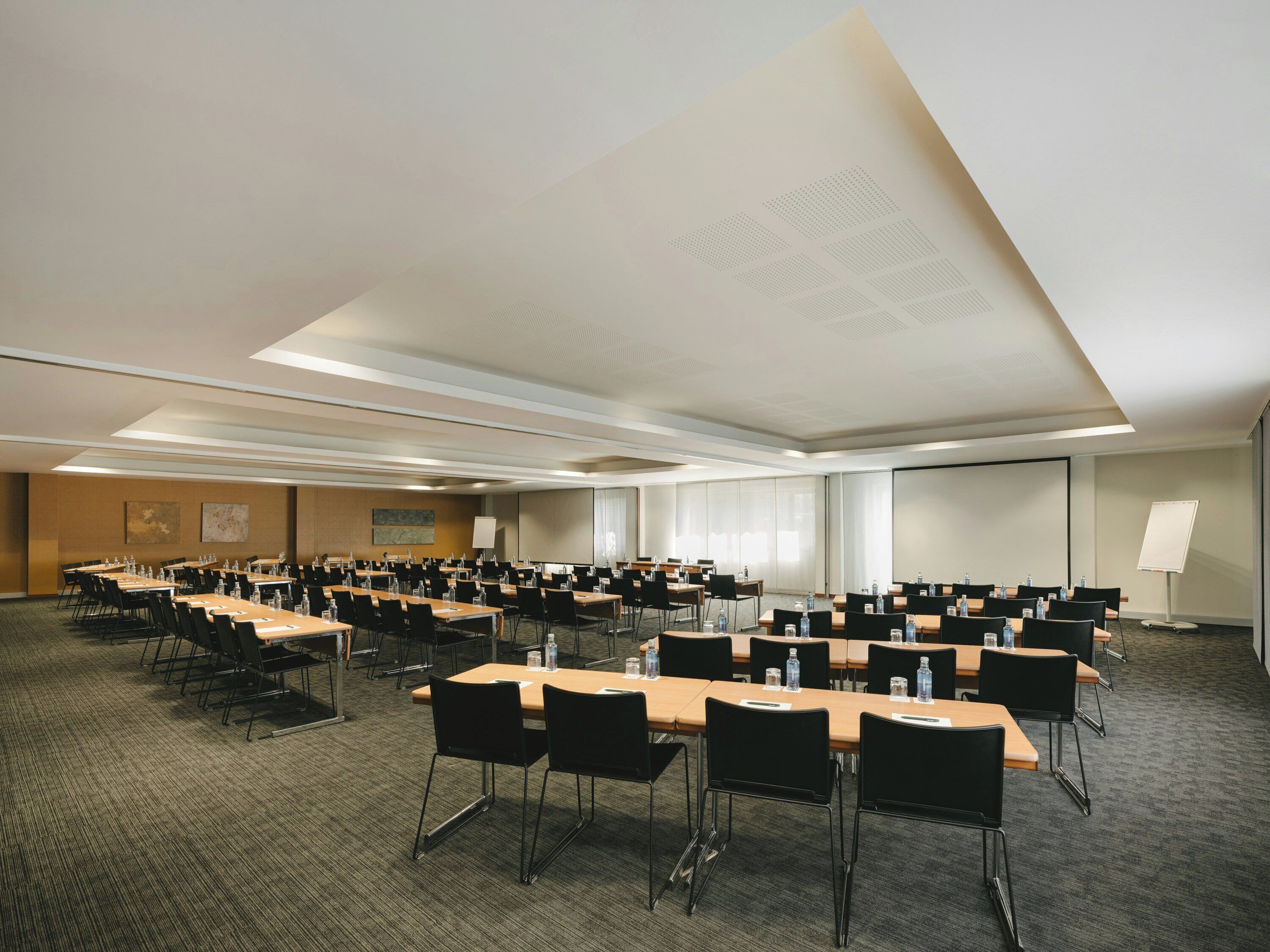 Sala de conferências com várias mesas e cadeiras, equipada com garrafas de água e placas de identificação.