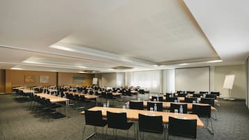 Sala de conferências com várias mesas e cadeiras, equipada com garrafas de água e placas de identificação.