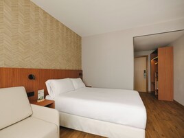 A hotel room with a bed, a nightstand, a chair, and a wardrobe.
