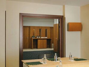 Une chambre d’hôtel avec une porte en bois, une petite kitchenette, une table recouverte d’une nappe verte et un miroir au mur.