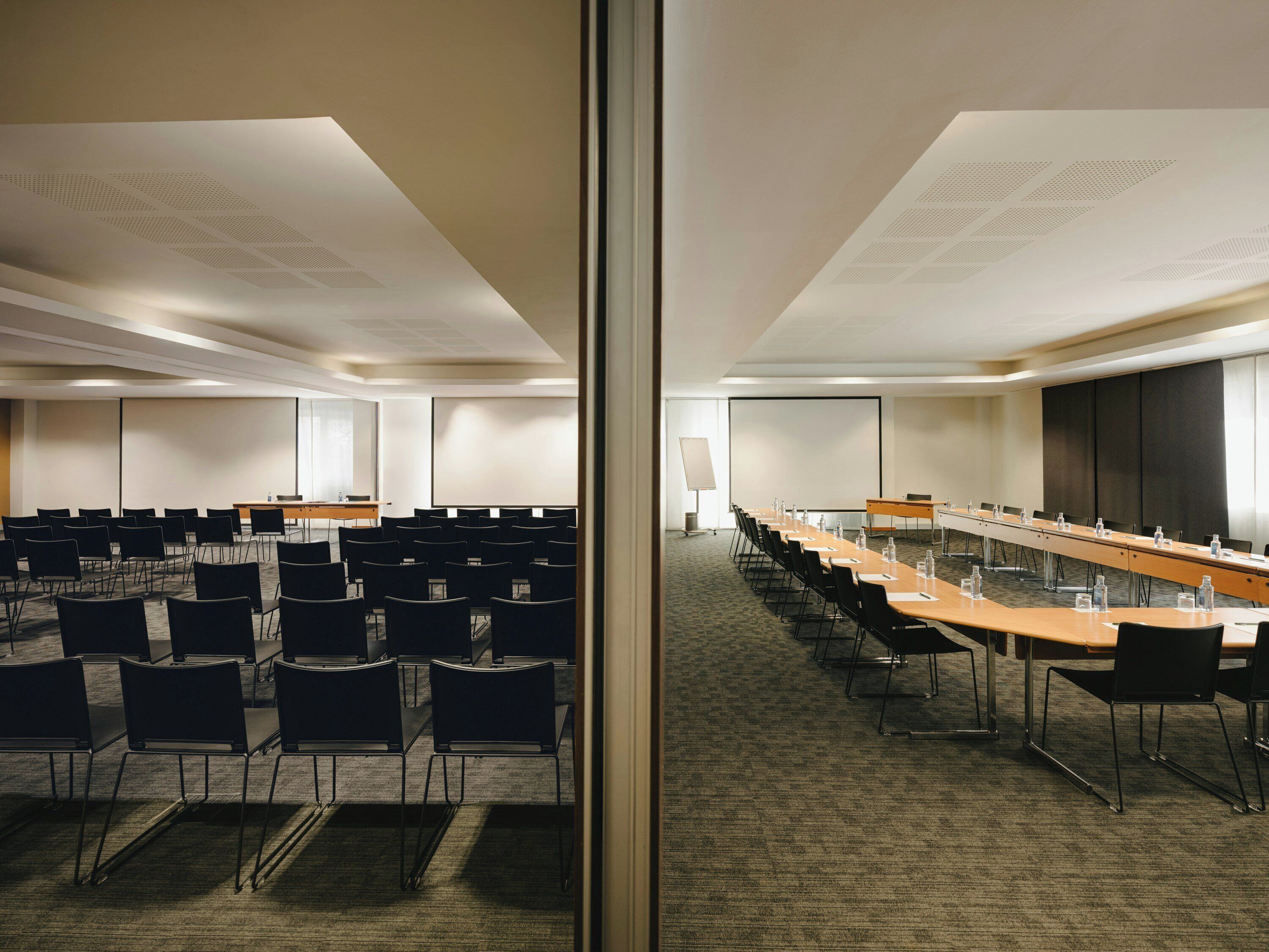 Un salón de conferencias con filas de sillas, una mesa larga y una pantalla para proyector.