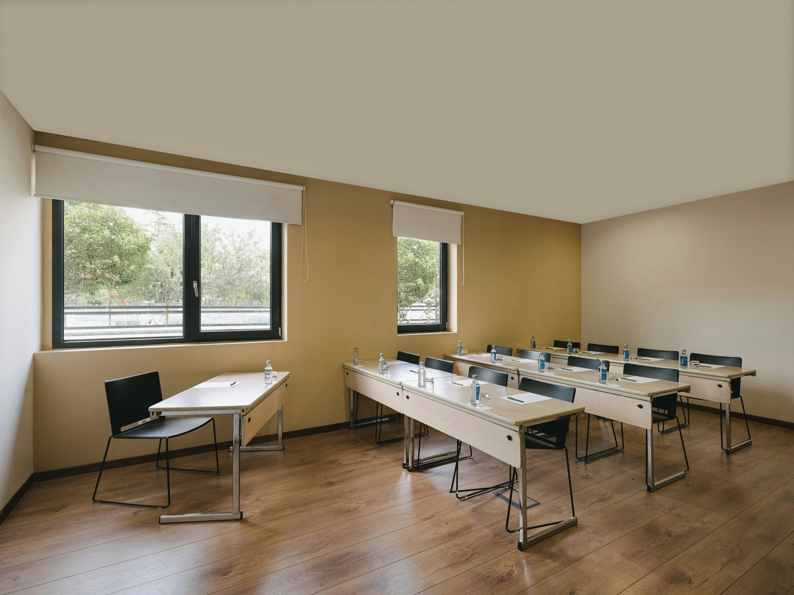 Une salle de conférence avec de longues tables, des chaises et une fenêtre équipée de stores.