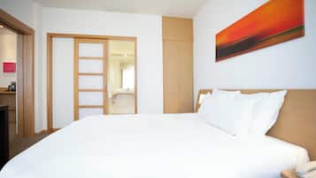Habitación de hotel con una cama grande, un armario de madera, un baño visible a través de una puerta abierta y un cuadro en la pared.