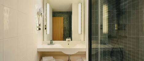 A modern bathroom with a white sink, a wooden shelf, a mirror, and a glass-enclosed shower area.