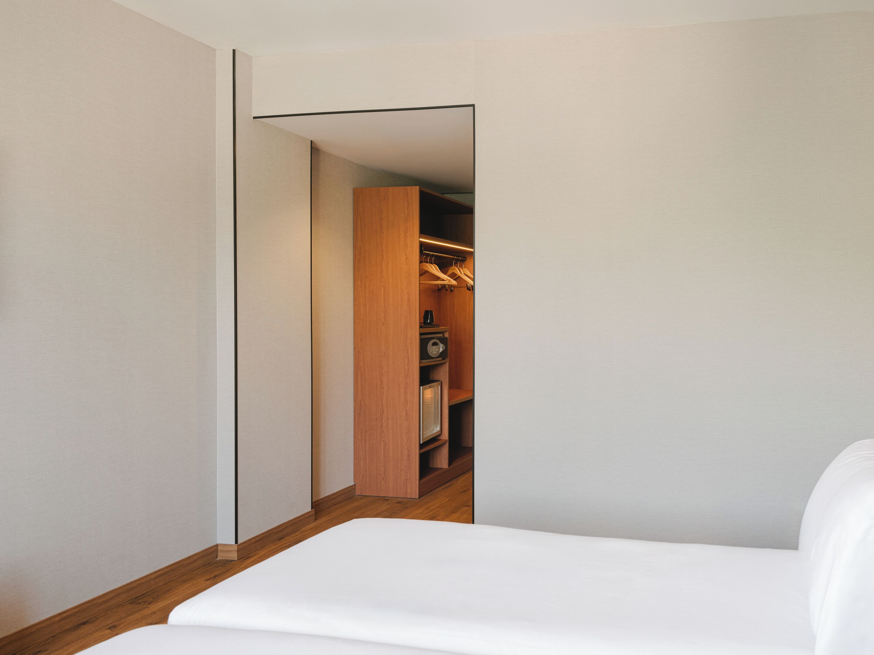 A narrow hallway leading to a closet with wooden doors and a hanging rack.