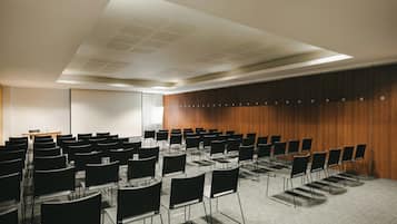 Una sala de conferencias con filas de sillas, una pantalla de proyector y un panel de pared de madera.