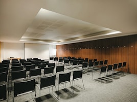Una sala de conferencias con filas de sillas, una pantalla de proyector y un panel de pared de madera.