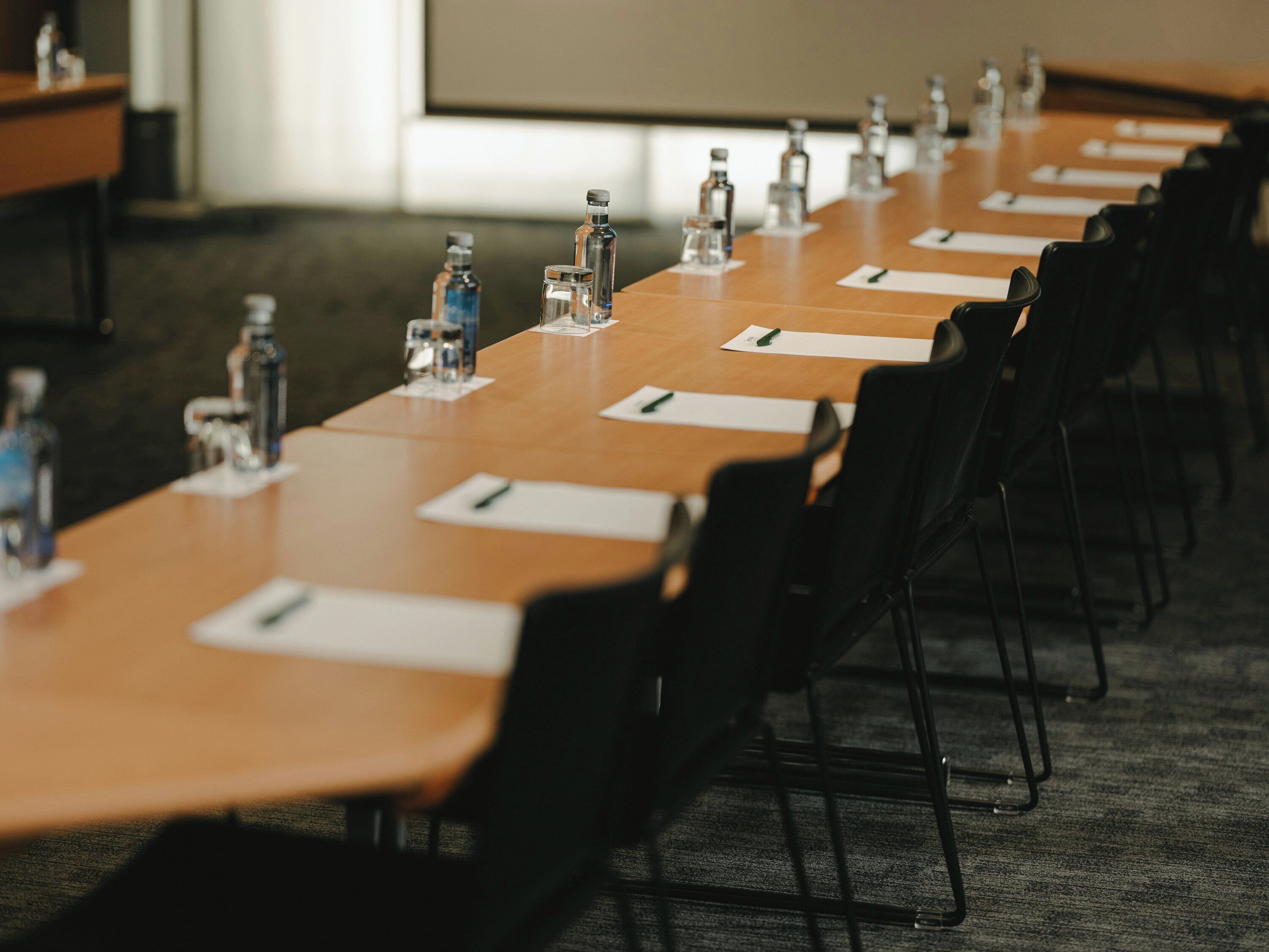 Una sala de conferencias con una mesa larga, sillas, botellas de agua y tarjetas de identificación.