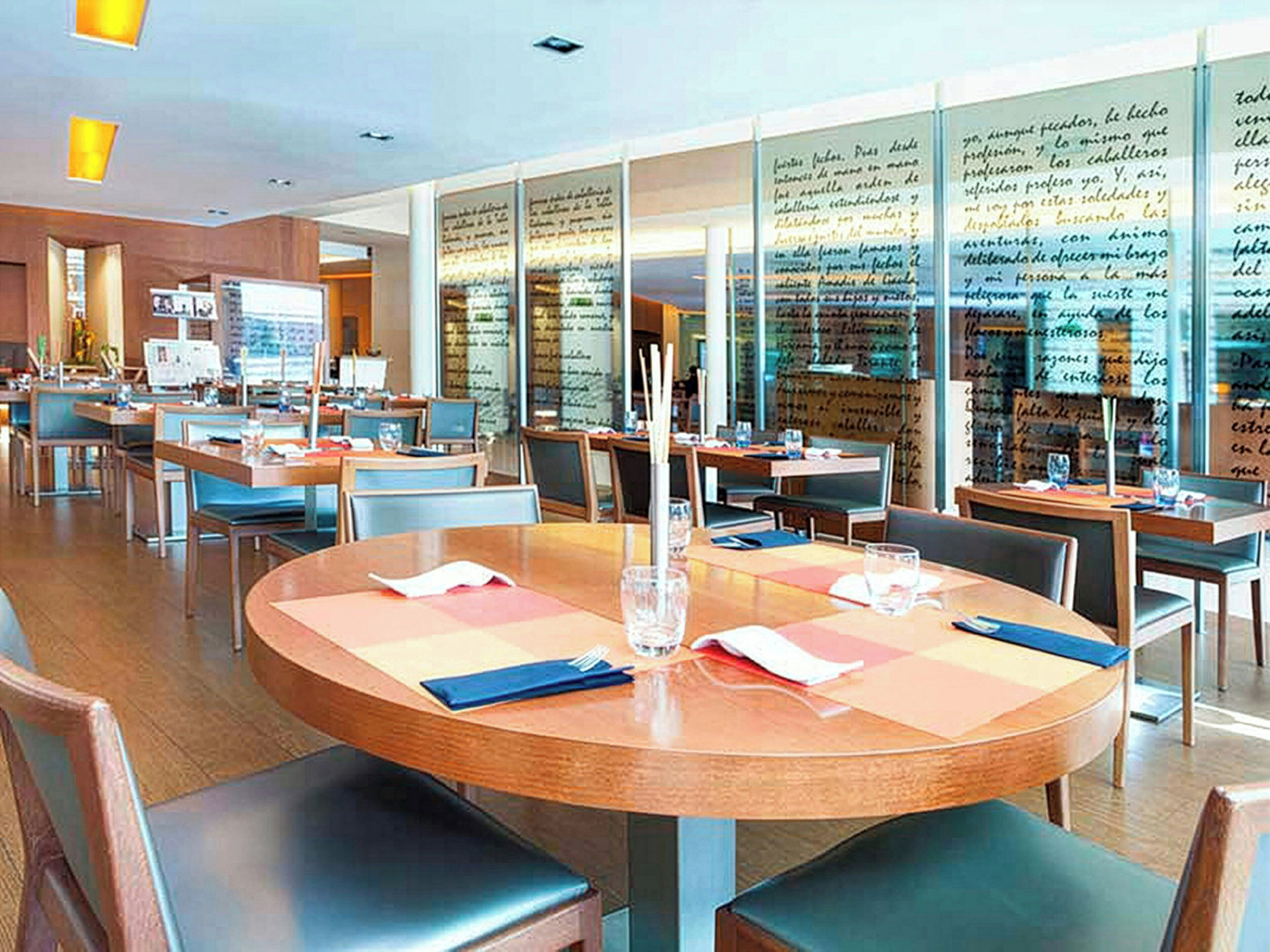 A restaurant with round tables, chairs, and a glass wall with writings.