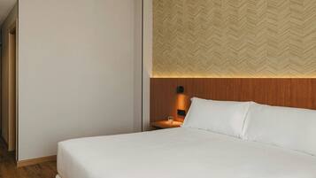 Habitación de hotel con cama, mesita de noche, pared con patrón de espiga y cabecera de madera.