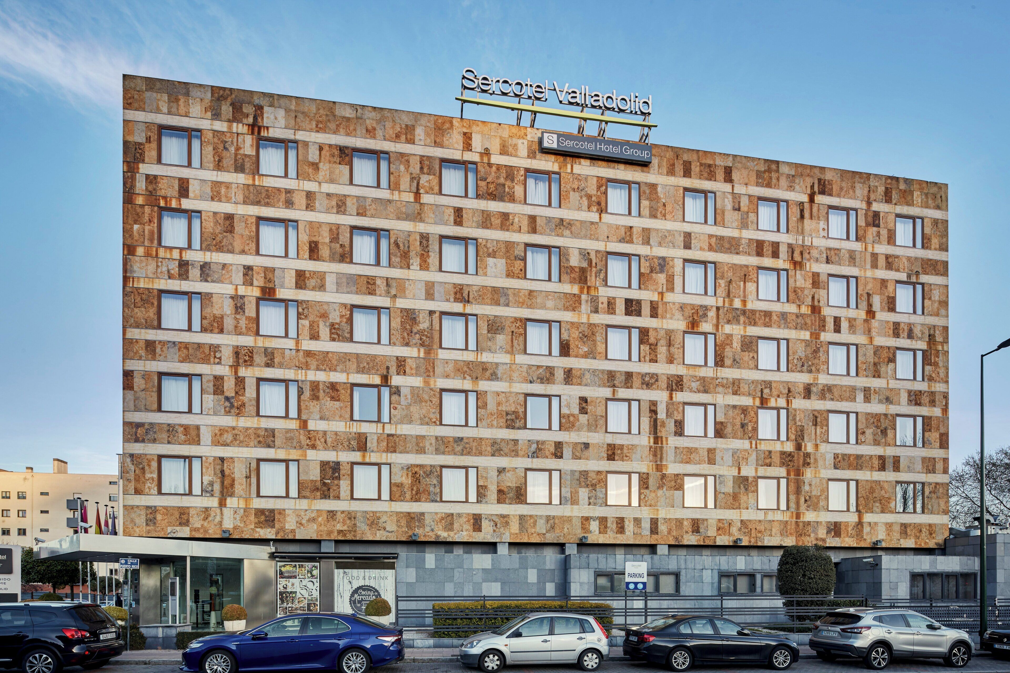 Een meerlaags hotel met een gedessineerde gevel, een bord dat aangeeft dat het deel uitmaakt van Serotel Hotel Group, en diverse geparkeerde auto's ervoor.