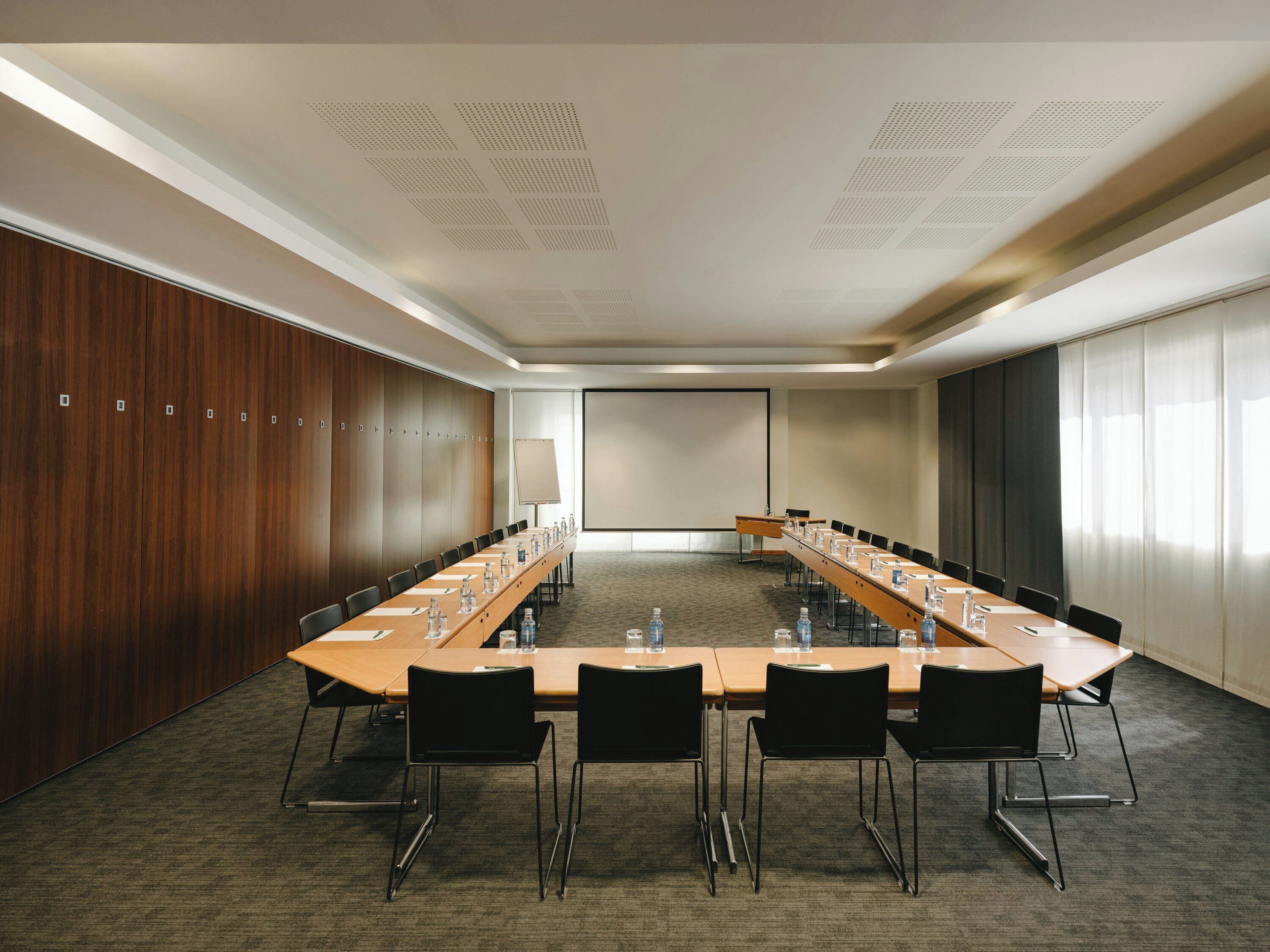 A conference room with a long table, chairs, water bottles, and a projector screen.