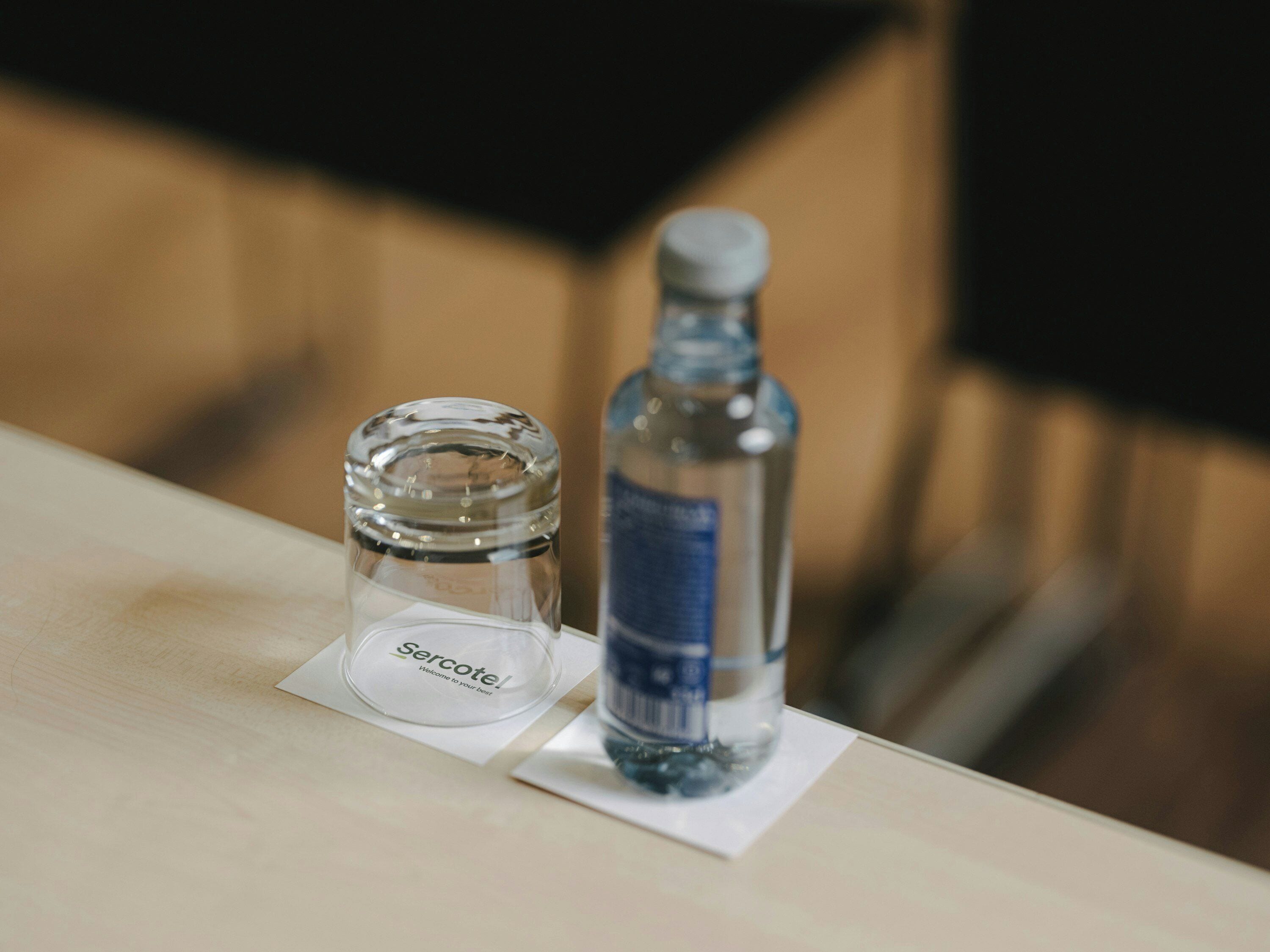 Una botella de vidrio transparente y un recipiente de vidrio más pequeño con una etiqueta sobre una superficie de madera.