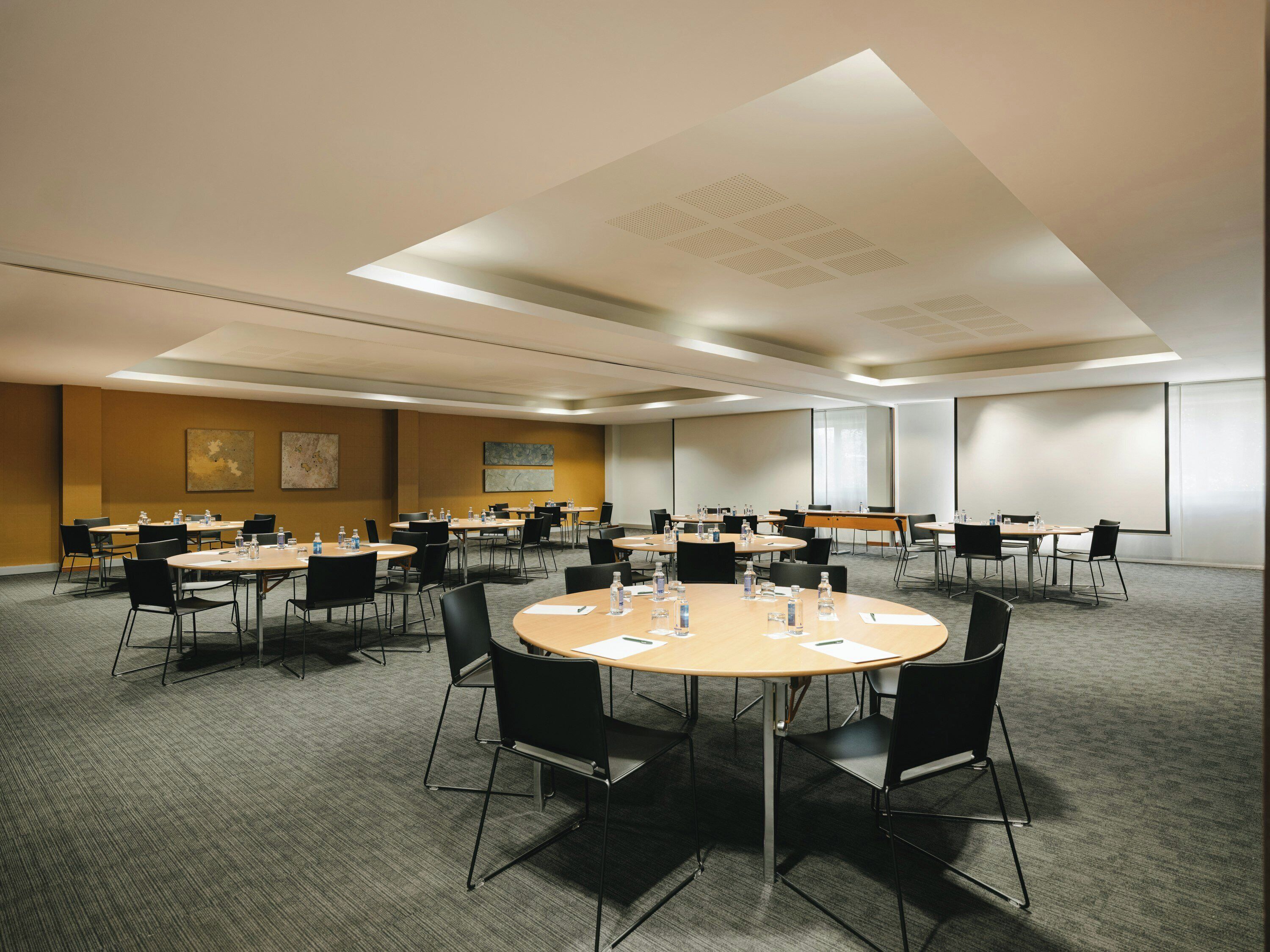 Uma sala de conferências com várias mesas e cadeiras, equipada com garrafas de água e papéis, em um ambiente moderno de hotel.