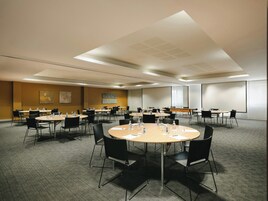 A conference room with multiple tables and chairs, equipped with water bottles and papers, in a modern hotel setting.