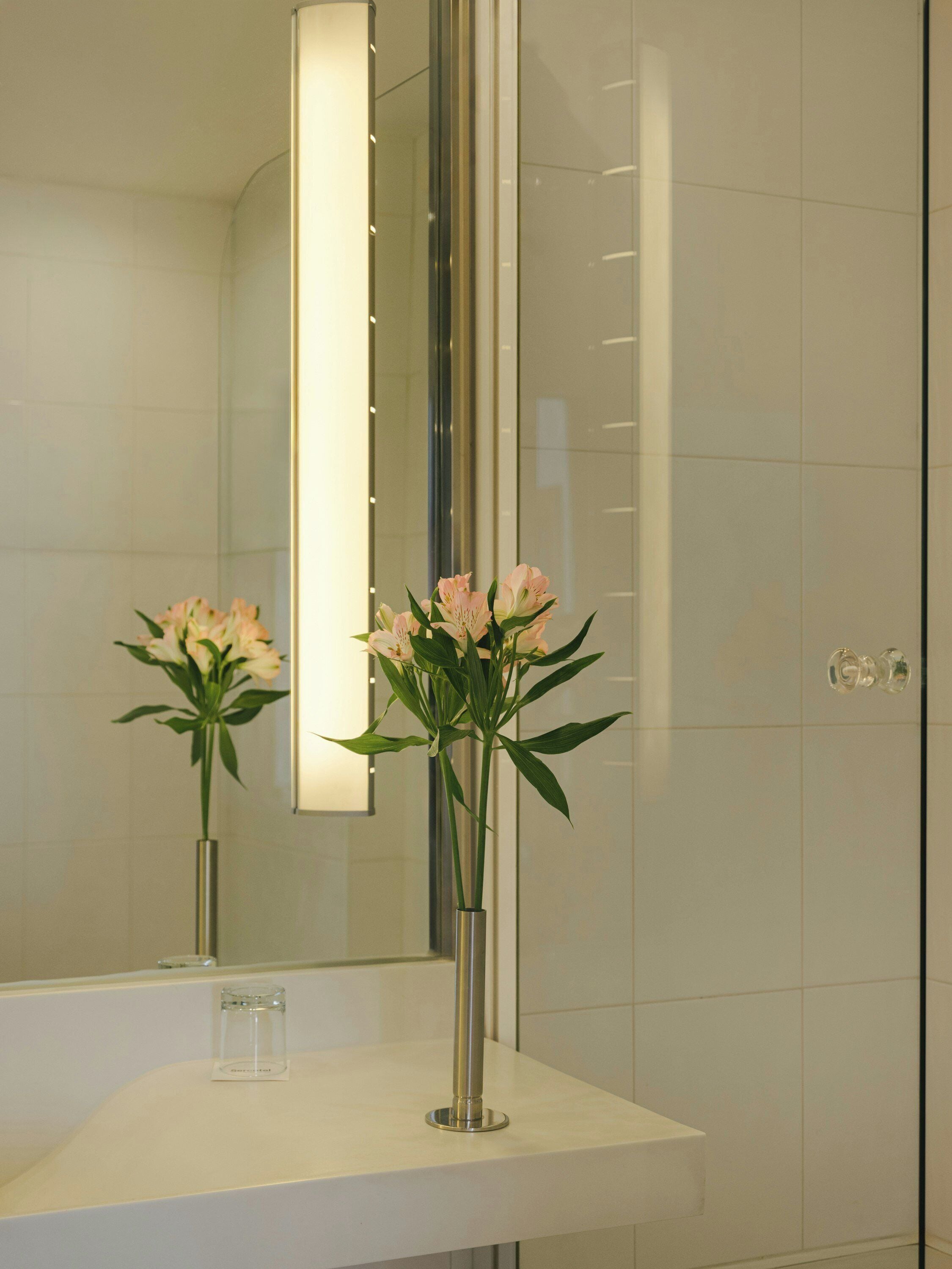 Un baño con un lavamanos blanco, un espejo y un florero con flores.