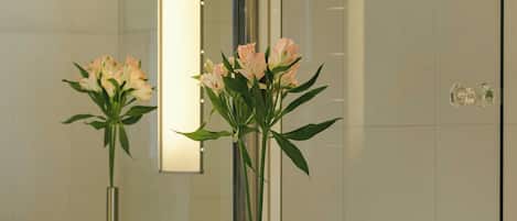 Un baño con un lavamanos blanco, un espejo y un florero con flores.