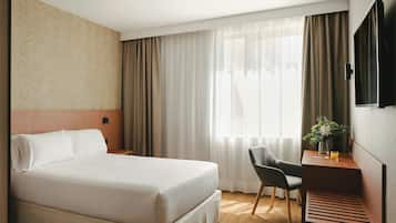 Een hotelkamer met een bed, een bureau, een stoel, een televisie en een raam met gordijnen.