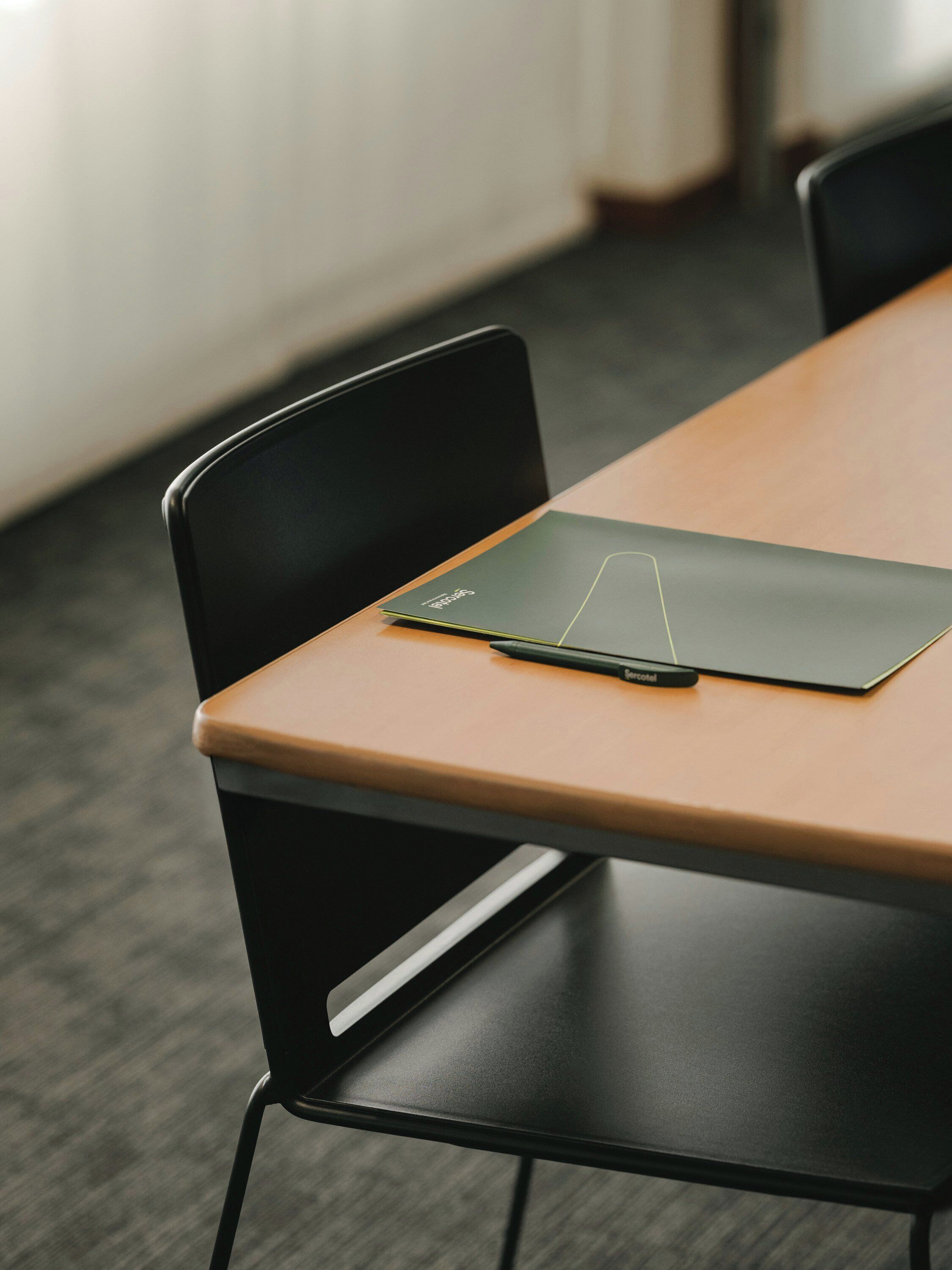 Une table de conférence avec une chaise noire, un dossier noir et un stylo dessus.
