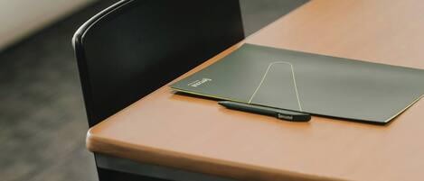 A conference table with a black chair, a black folder, and a pen on it.