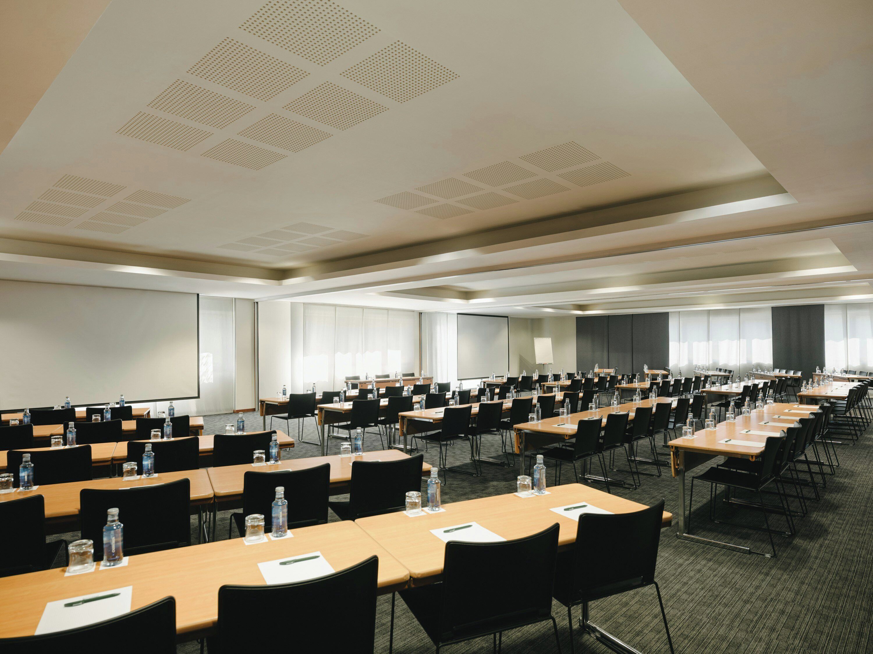 A conference room with multiple tables, chairs, and a large screen.