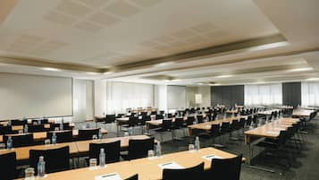 A conference room with multiple tables, chairs, and a large screen.