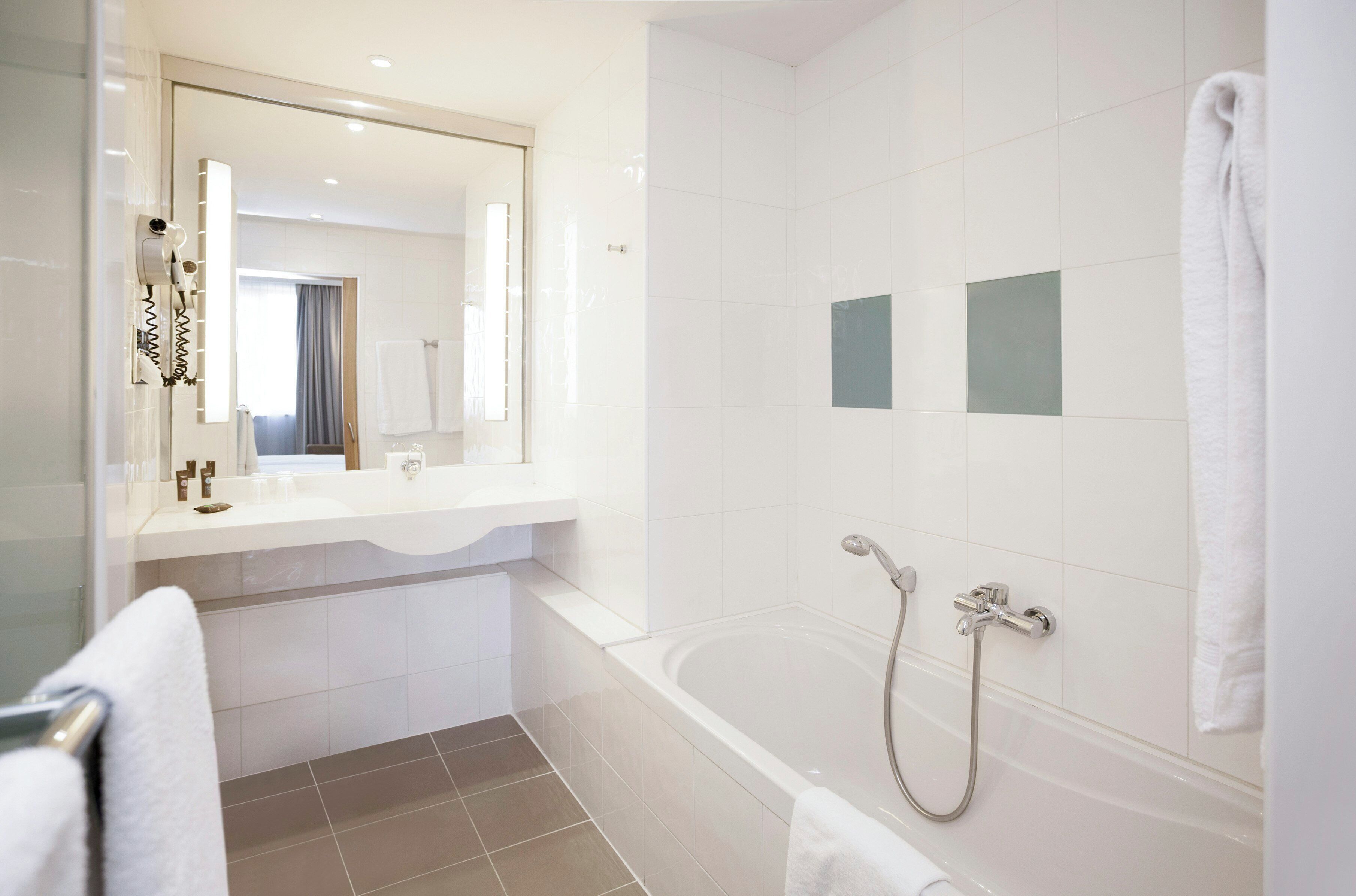 A modern bathroom with a large mirror, a bathtub, and a shower area.