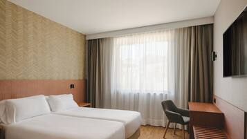 Una habitación de hotel con dos camas, un escritorio, una silla, un televisor y una ventana con cortinas.