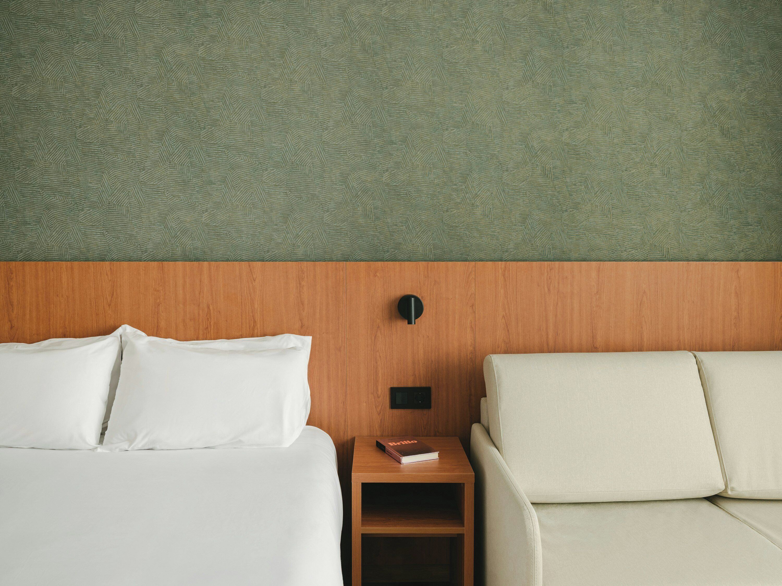 Une chambre d’hôtel avec un lit, une table de chevet, un livre et un canapé.