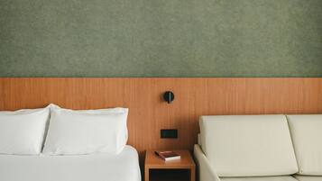 Una habitación de hotel con una cama, una mesita de noche, un libro y un sofá.