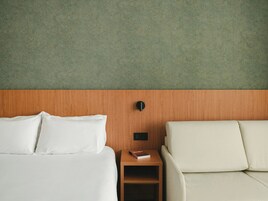 Una habitación de hotel con una cama, una mesita de noche, un libro y un sofá.