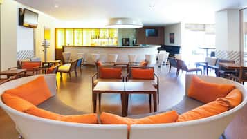 Um saguão de hotel moderno com um sofá curvo, mesas de jantar e um bar.